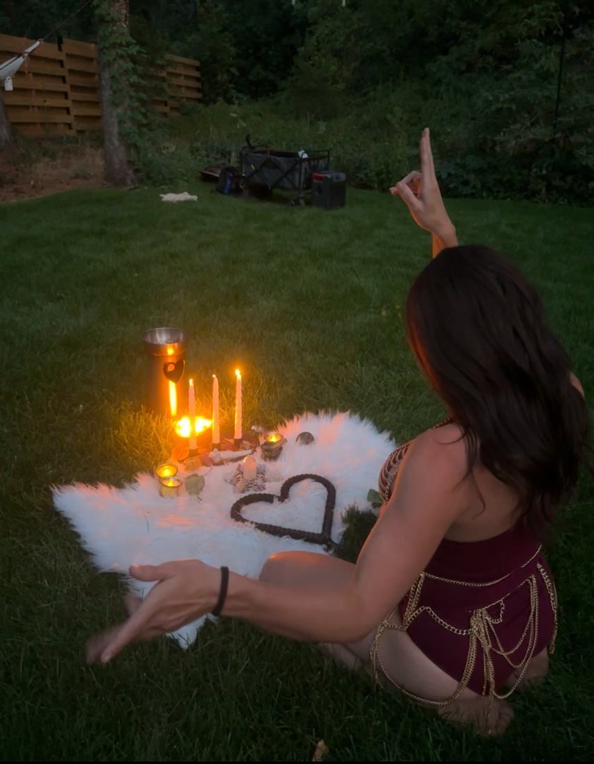 A ceremony altar of candles, crystals and a heart-shaped fire staff on a white fur rug at dusk