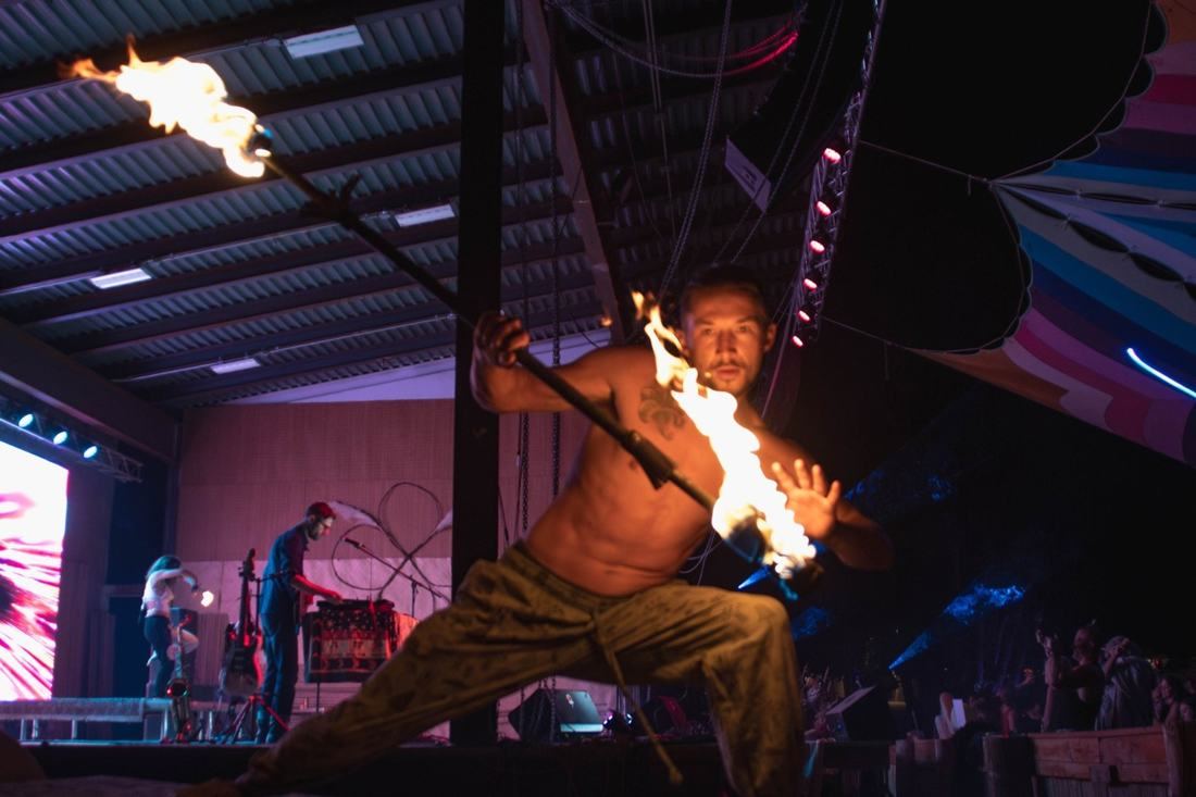 Tyler in a low stance spinning a fire staff on a festival stage