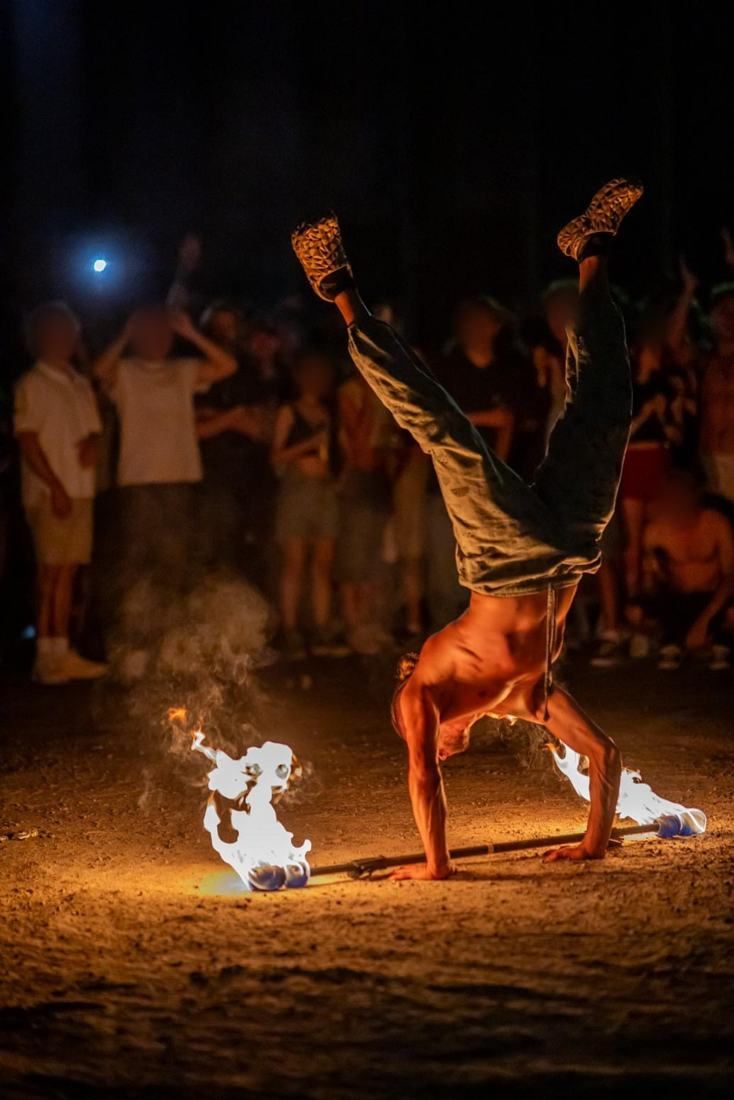 Tyler in a handstand over a burning fire staff in front of a festival crowd