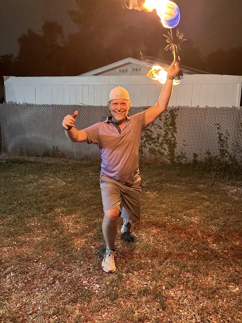 A man giving a thumbs up and beaming as he holds a lit fire staff