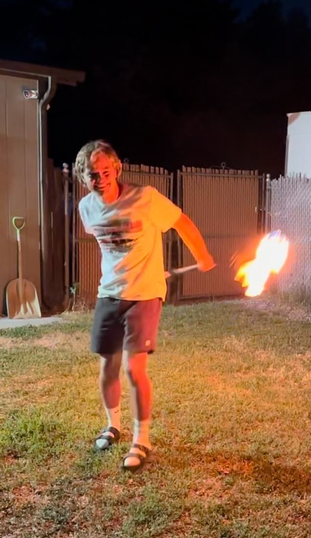 A young man laughing as he spins fire