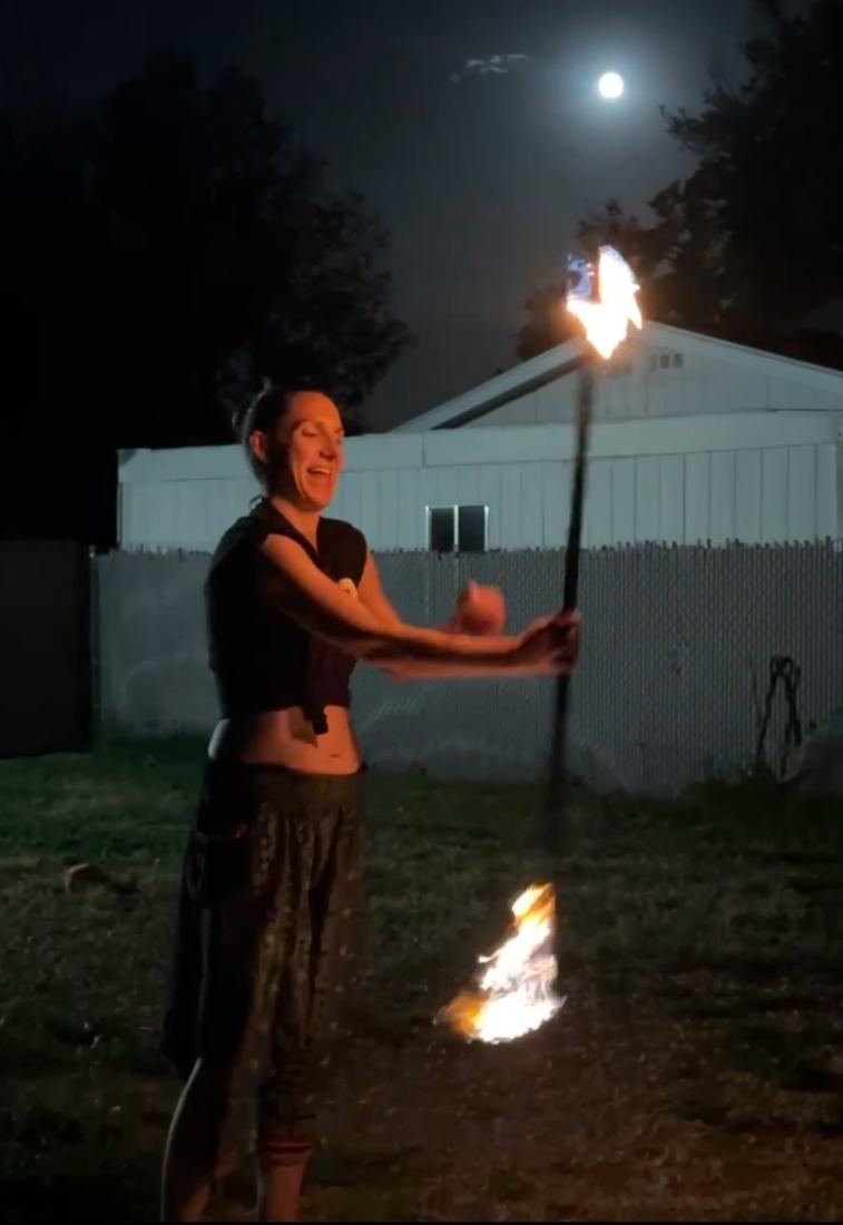 A woman spinning a fire staff under the full moon