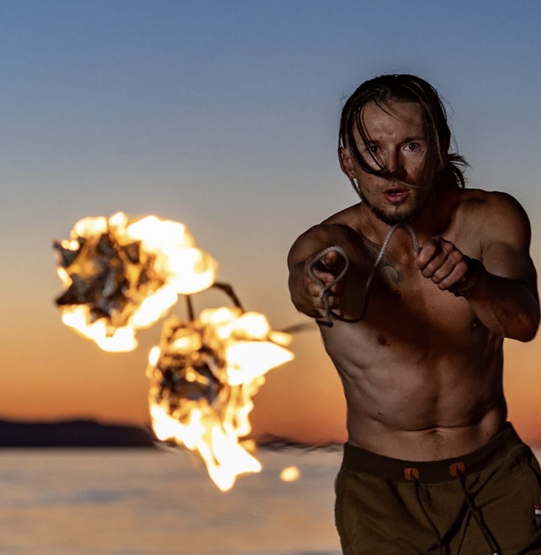 Tyler swinging flaming rope darts toward the camera at sunset on the lake