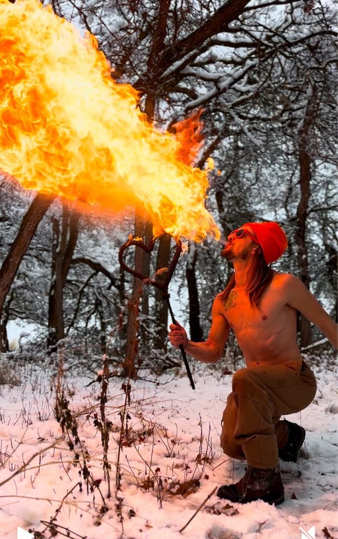 Tyler kneeling in snowy woods breathing a huge fireball over a heart staff
